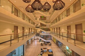 A multi-level hotel lobby with glass railings, a central staircase, and modern furnishings. - Lime Resort El Nido (El Nido)