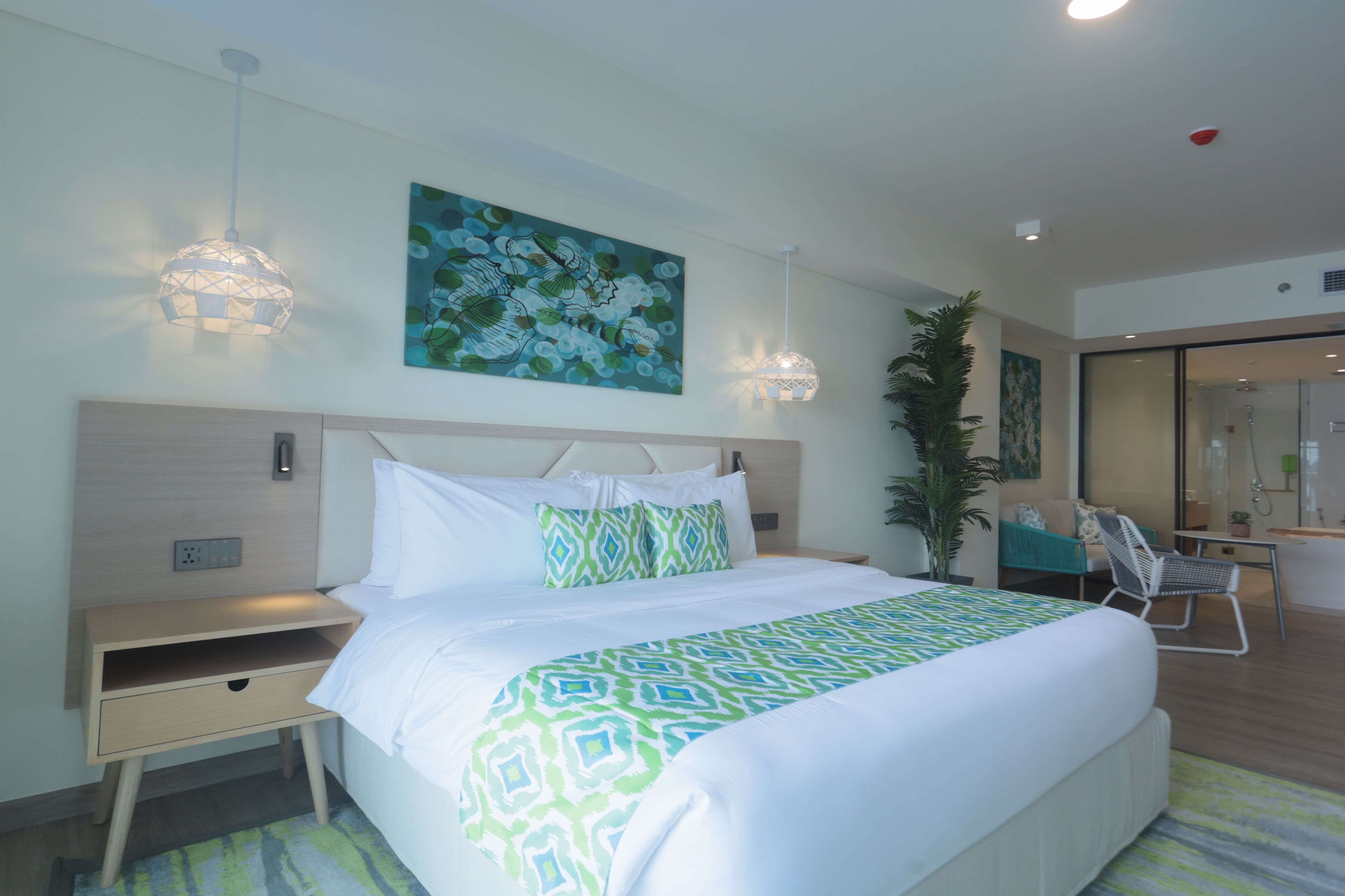 A modern hotel room with a large bed, a nightstand, a desk, and a chair.