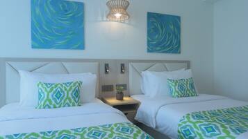 A hotel room with two beds, a nightstand with a lamp, and two abstract paintings on the wall.