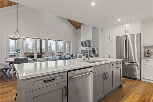 A modern kitchen with a large island, stainless steel appliances, and a dining area with a view of trees.