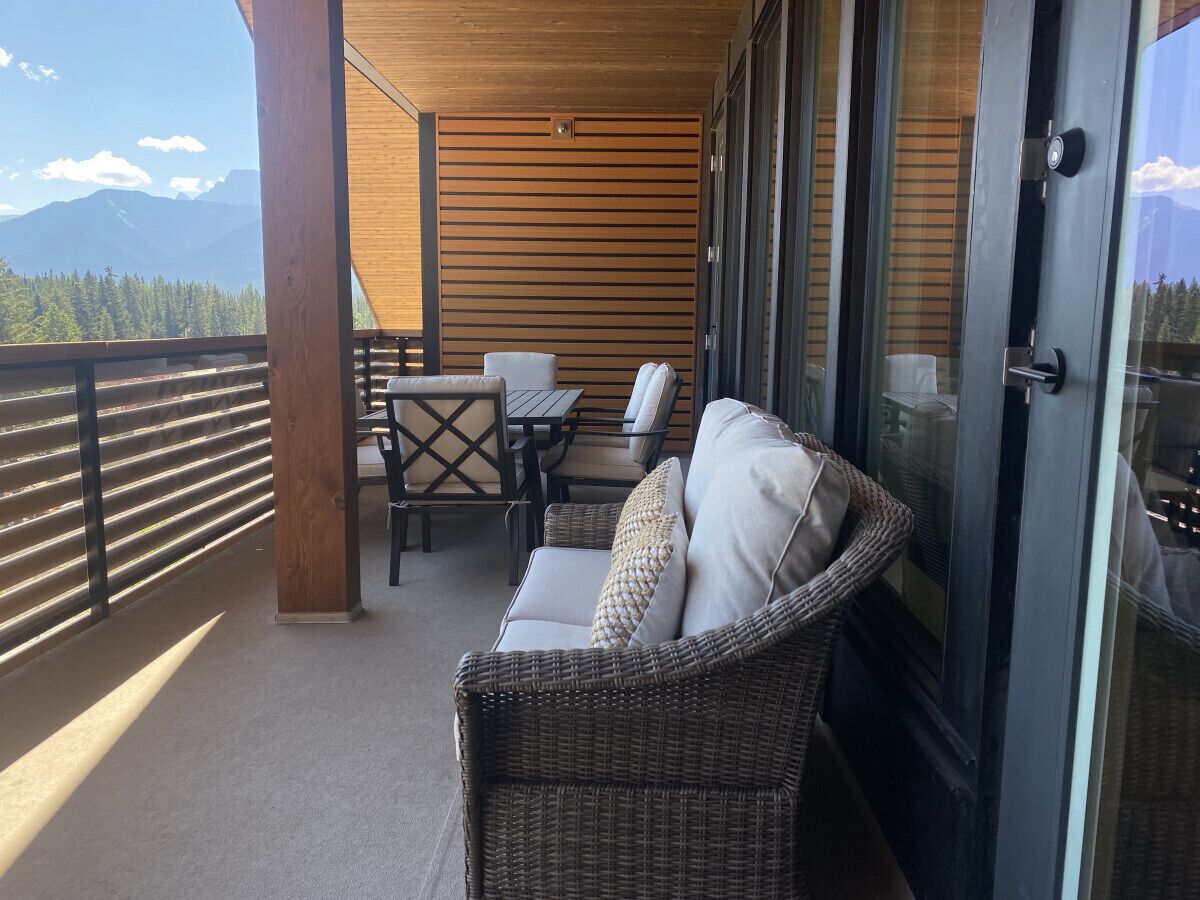 Un balcón con un sofá de mimbre, una mesa y sillas, con vista a un paisaje montañoso.