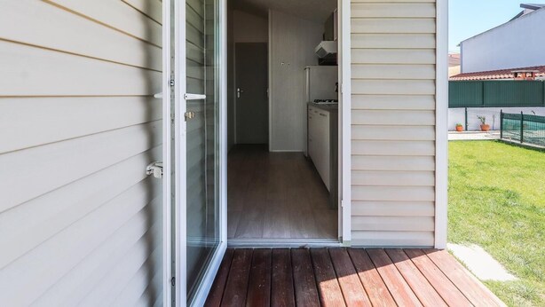 Ein kleiner, abgeschlossener Balkon mit Holzterrasse, eine Schiebetür zu einer kompakten Küche mit Kühlschrank und Schränken.
