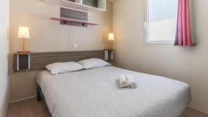 Ein ordentlich eingerichtetes Hotelzimmer mit einem großen Bett, zwei Nachttischen mit Lampen, einer eingebauten Ablage über dem Bett und einem Fenster mit Vorhängen.