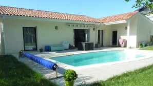Piscina residencial con techo de azulejos, carrete de manguera cubierto y una planta en maceta.