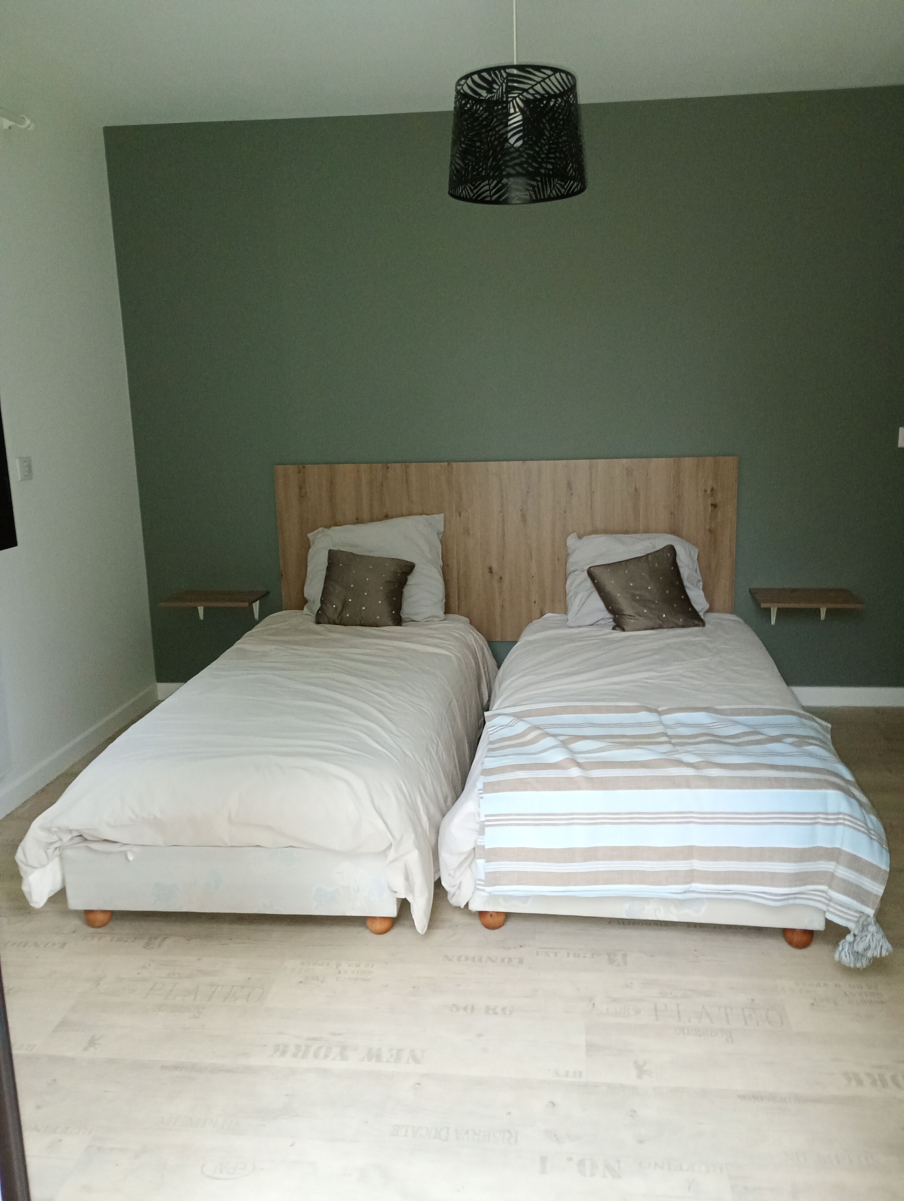 Une chambre avec deux lits, une tête de lit en bois et un luminaire suspendu.
