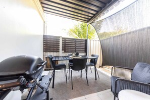 A covered patio area with a table and chairs, a grill, and a screened area. - Urban Getaway Whole Home - 6BR/5BA, Sauna, Ipswich (Newtown)
