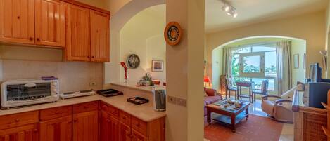 A kitchen with wooden cabinets, a toaster, and a coffee maker. There is a dining area with a table, chairs, and a TV.
