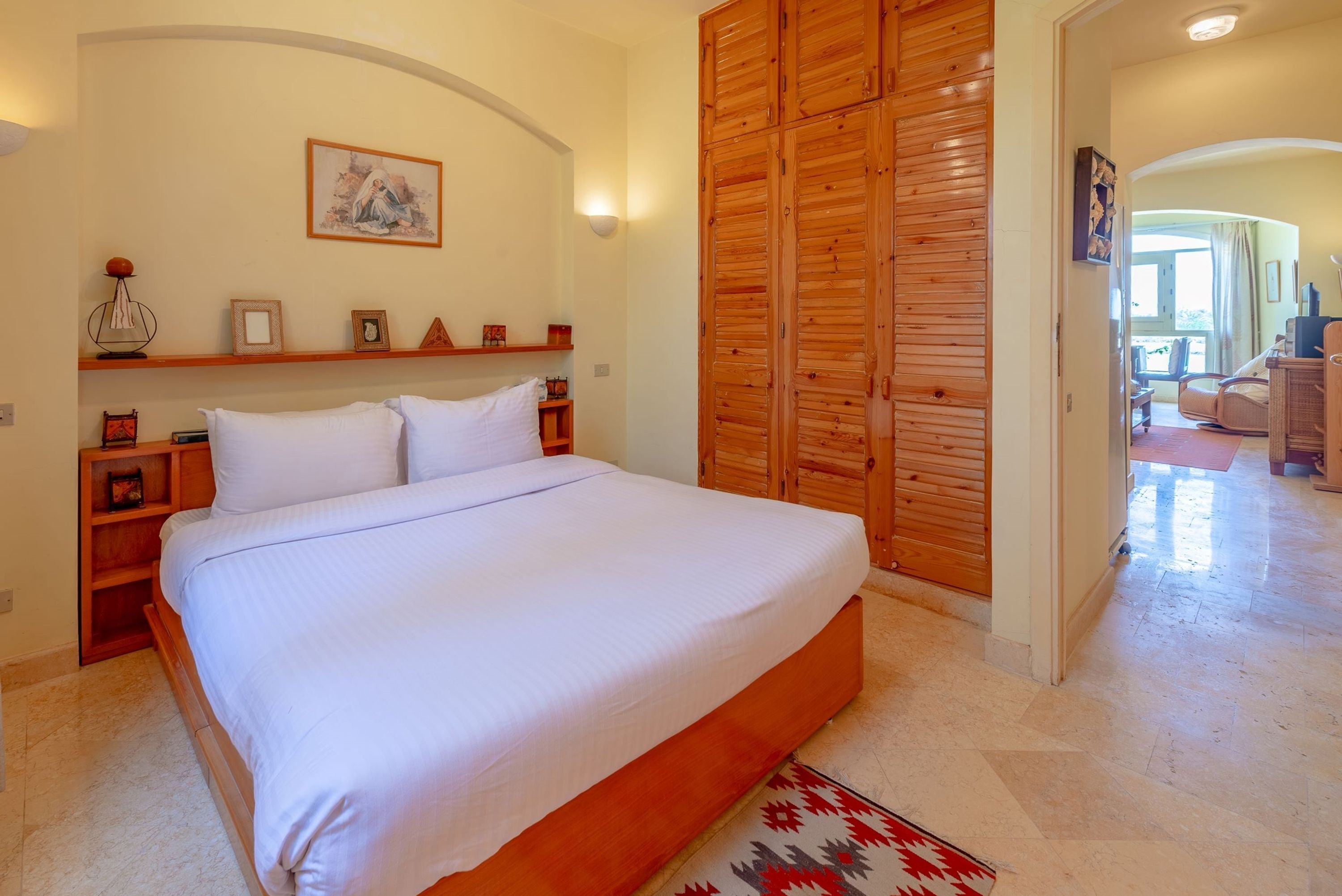 Un dormitorio con una cama grande, un armario de madera y una pequeña estantería con fotografías enmarcadas.