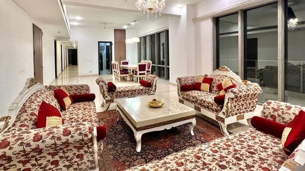 A spacious living room with a chandelier, patterned sofas, and a large window. - Entire Luxury 2BHK Flat for Parties/ Family (New Delhi)
