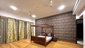 A bedroom with a four-poster bed, wooden flooring, a patterned wall, and ceiling fans. - Entire Luxury 2BHK Flat for Parties/ Family (New Delhi)