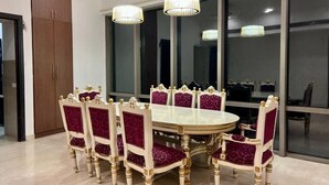 A dining area with a round table and eight chairs, each with a high back and cushioned seat. - Entire Luxury 2BHK Flat for Parties/ Family (New Delhi)