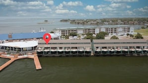 Un hotel frente al agua con un muelle, un edificio grande con varios balcones y un puerto deportivo con barcos.