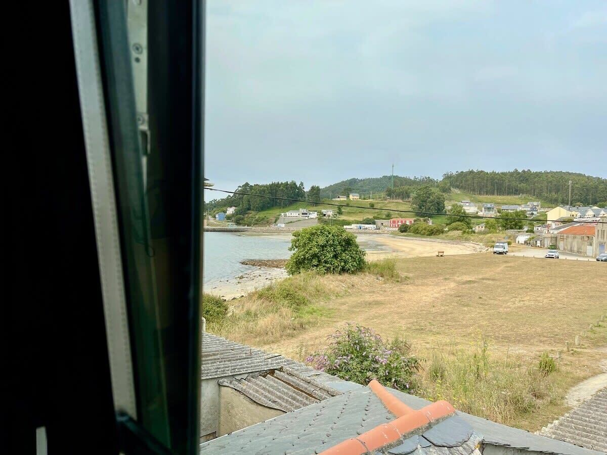 A view from a window overlooking a river, a grassy field, and a few buildings in the distance.