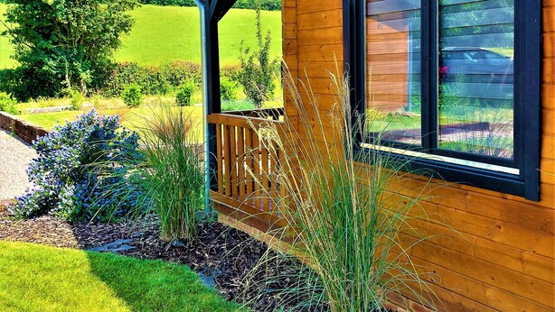 A wooden cabin with a porch, a window, and a view of a green field.