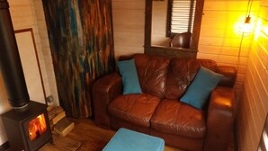 A cozy living room with a brown leather sofa, blue cushions, a small blue ottoman, a wood-burning stove, and a mirror above the sofa.