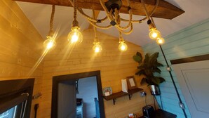 A rustic interior with exposed wooden beams, a ceiling light fixture with multiple bulbs, and a potted plant.