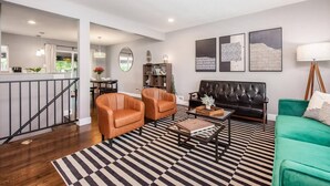 A modern living room with a black leather sofa, two brown leather armchairs, a green sofa, a coffee table, and a striped rug. There is a bookshelf, a mirror, and artwork on the walls.