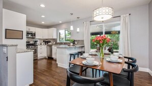 A modern kitchen with white cabinets, a central island, and a dining area with a wooden table and black chairs.