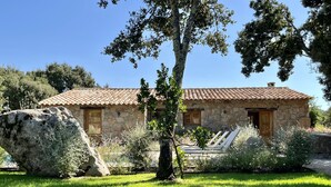 Une maison en pierre avec un toit en tuiles, un grand rocher au premier plan et une pelouse bien entretenue.