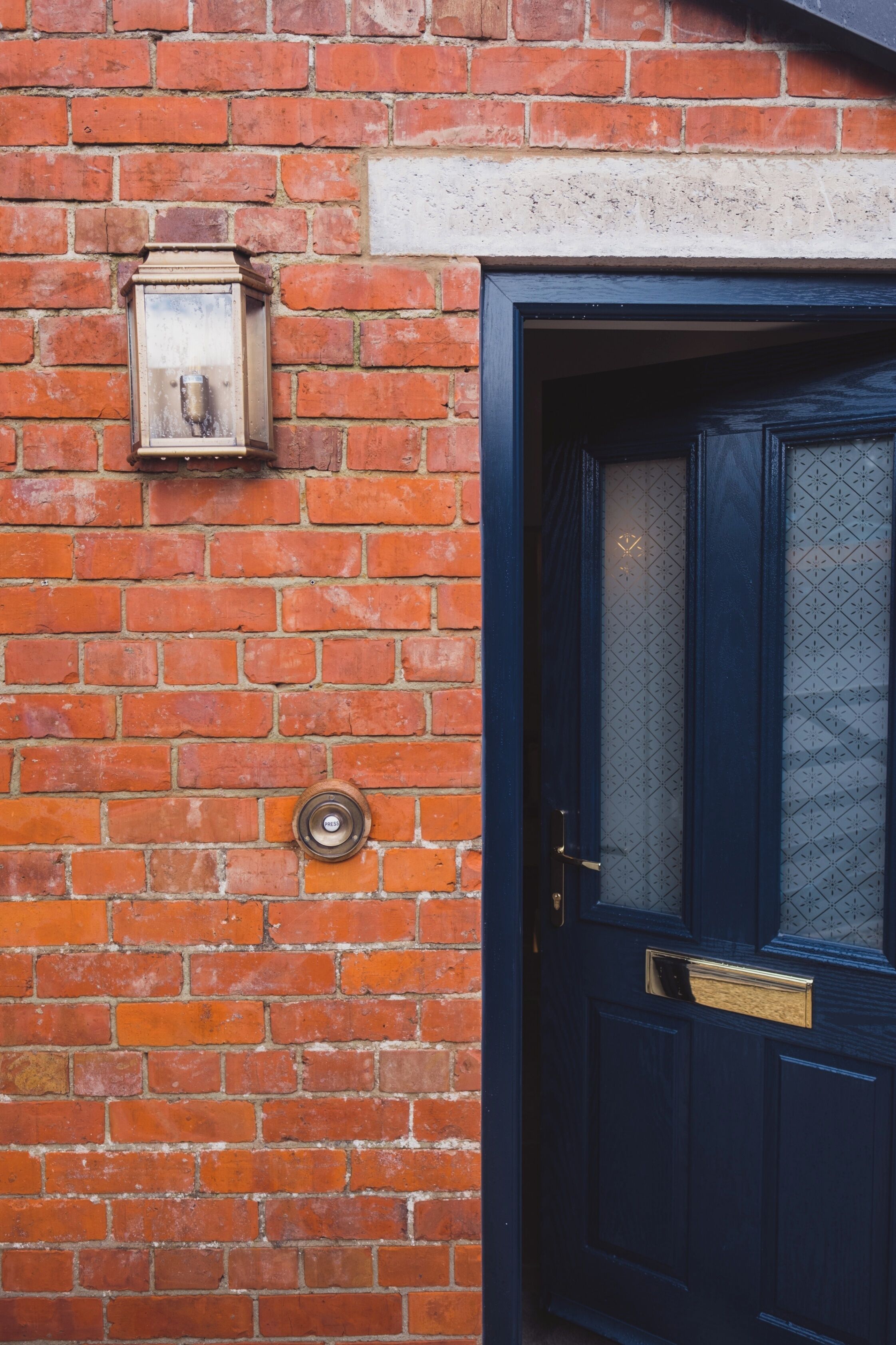 A brick wall with a blue door, a brass door knocker, and a small, rectangular, light fixture.