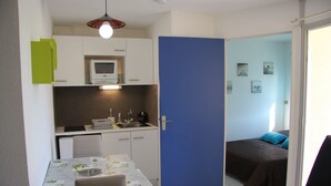 Een compacte kamer met kitchenette, een eethoek en een bed.