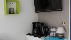 Een kitchenette met een koffiezetapparaat, een televisie erboven en een klein plankje met een decoratief object.