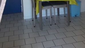 Een eetruimte met een tafel bedekt met een gele tafelkleed, twee stoelen, een plafondventilator en twee ingelijste foto's aan de muur.