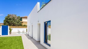 A modern building with a white exterior, a blue door, and a small pool area with lounge chairs.