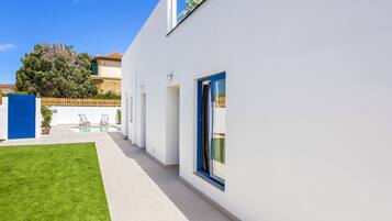 Een modern gebouw met een witte gevel, een blauwe deur en een klein zwembadgedeelte met ligbedden.