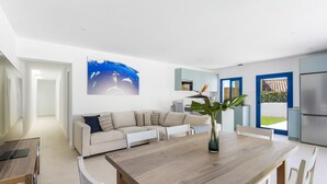 A modern living room with a wooden dining table, white sofa, and a large painting of dolphins.