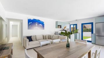 Un salon moderne avec une table à manger en bois, un canapé blanc et un grand tableau représentant des dauphins.