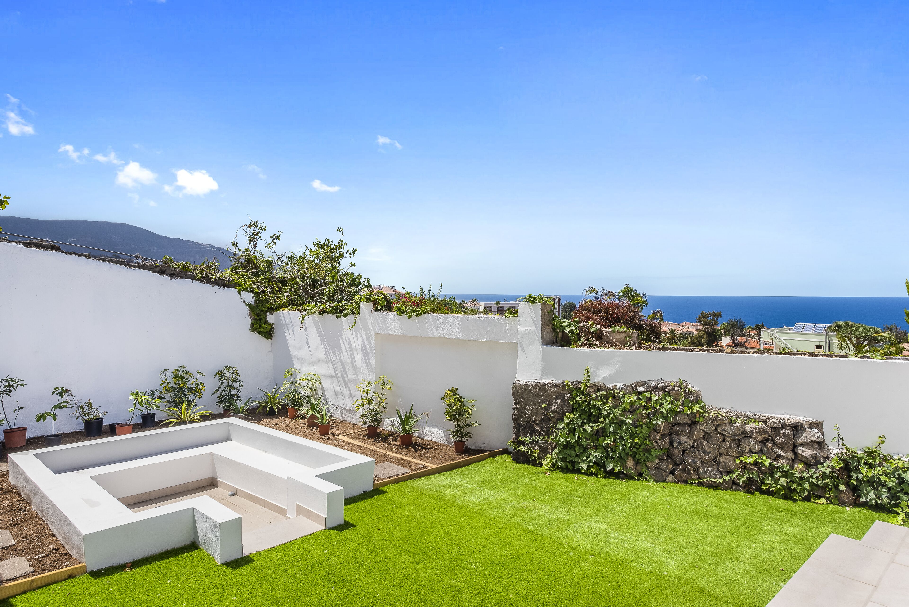 A landscaped garden with a white wall, a stone wall, and a variety of potted plants.