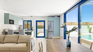 A modern kitchen with a dining area, large windows, and a view of the outdoors.