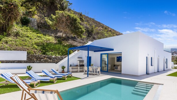 A modern house with a swimming pool, outdoor seating, and a view of a hillside.