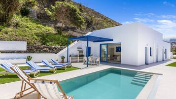 Une maison moderne dotée d’une piscine, d’un espace salon extérieur et offrant une vue sur une colline.