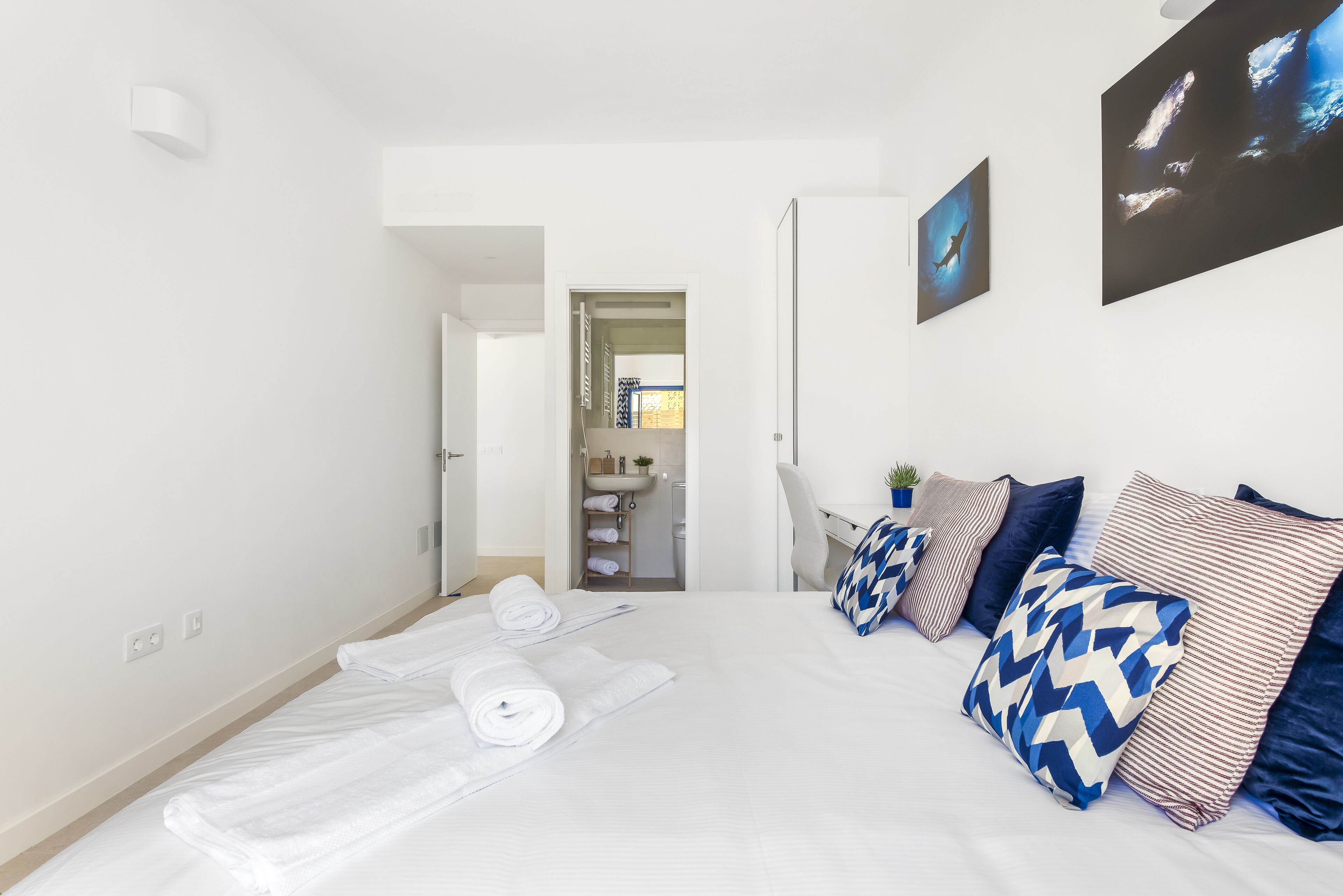 Habitación de hotel moderna con una cama bien hecha, un baño visible a través de una puerta abierta y vistas al cielo por una ventana.