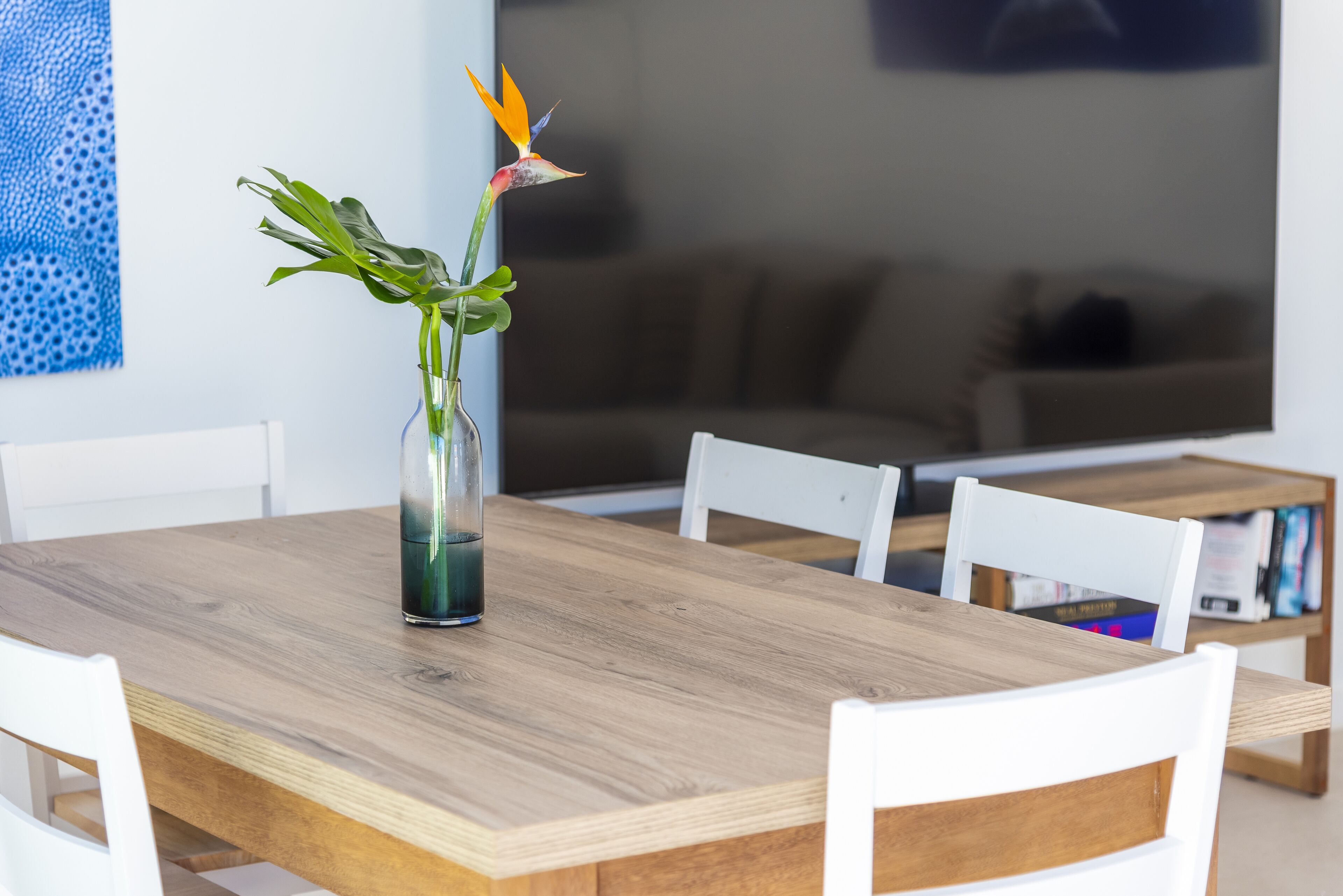 A wooden dining table with a clear glass vase containing a bird of paradise flower.