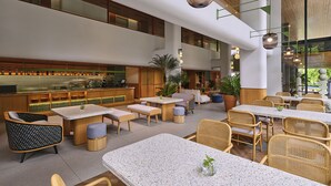 Um espaço amplo e interno com diversas opções de assento, incluindo mesas e cadeiras, e uma área de bar com balcão e prateleiras.