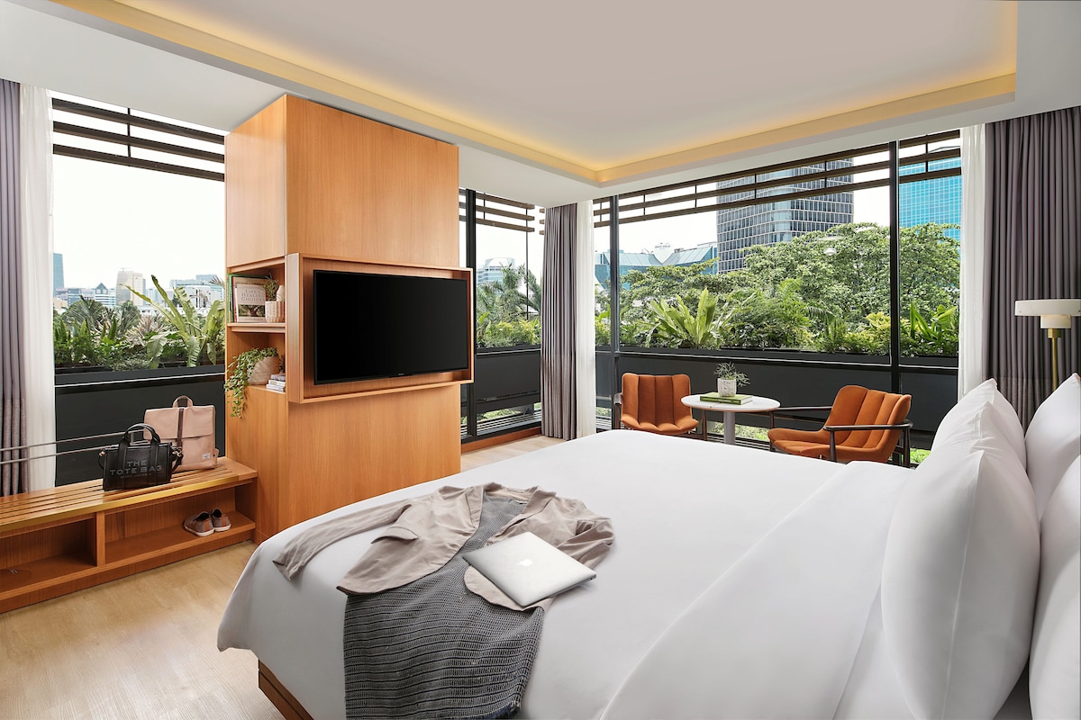 A hotel room with a large bed, a TV mounted on the wall, a small table, and a chair.