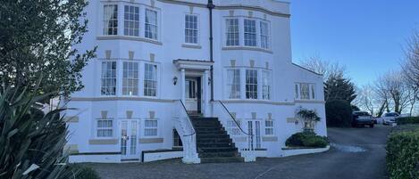 A large, white, two-story building with a central entrance and a staircase leading to the upper floor.