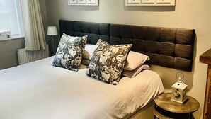 Uma cama bem arrumada com almofadas estampadas em flor, uma cabeceira escura e arte botânica emoldurada na parede.