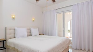 Ein Schlafzimmer mit einem großen Bett, zwei Nachttischen, einem Deckenventilator und einer Glastür, die zu einem Außenbereich führt.