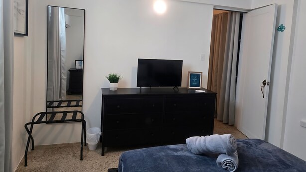 Une chambre à coucher moderne avec un lit, un téléviseur posé sur une commode, une petite plante et un miroir.
