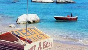 Een strand met een vlag, een boot en een bord waarop staat 'Rent A Boat'.