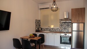 Een praktische keuken met een eethoek, inclusief een tafel met stoelen, een koelkast, een oven en een hangende lamp.