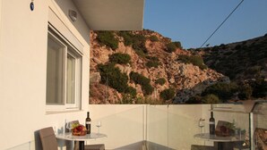 Een balkon met twee tafels, elk met een fles wijn en een glas, en rieten stoelen.