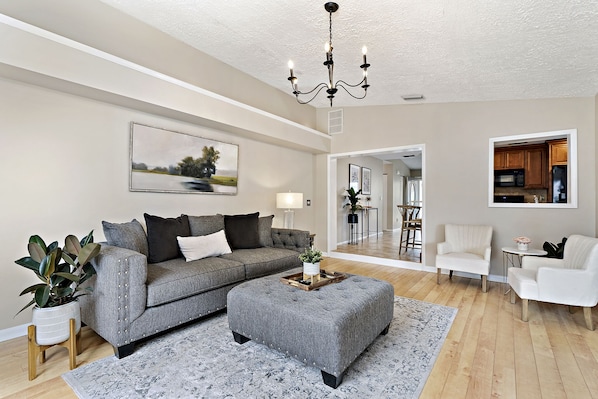 A living room with a grey sofa, a grey ottoman, a white armchair, and a small table with a lamp.