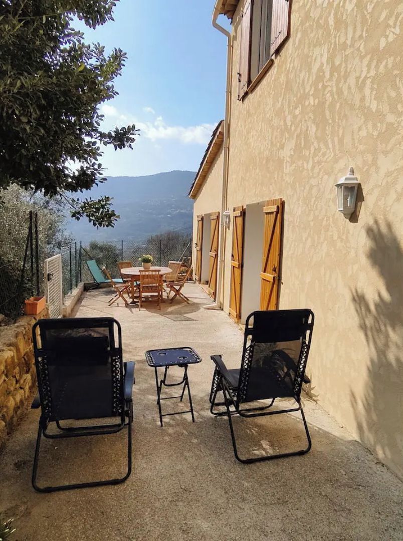 Une terrasse extérieure avec une table et des chaises, un mur en pierre et une vue sur les montagnes.