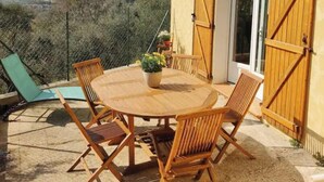 An outdoor patio with a round wooden table and chairs, a wooden door, and a view of a mountainous landscape. - Bas de Villa - Nice hinterland (Contes)