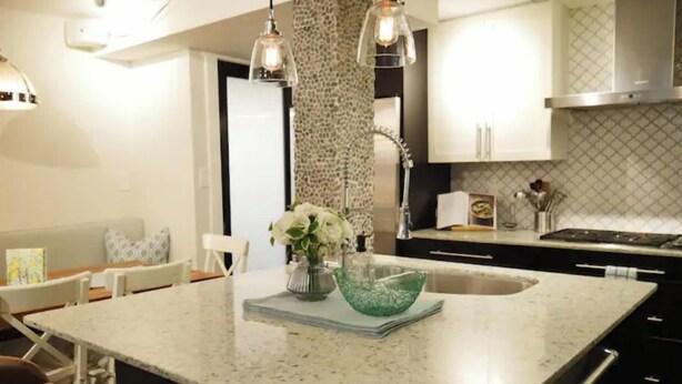 Una cocina con una isla grande, armarios blancos e iluminación colgante.